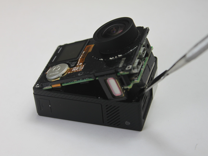 Passo 3 Para remover o conjunto da placa-mãe do invólucro da câmara, utilize a ferramenta de abertura de plástico no lado da lente da câmera para erguer a montagem da placa-mãe