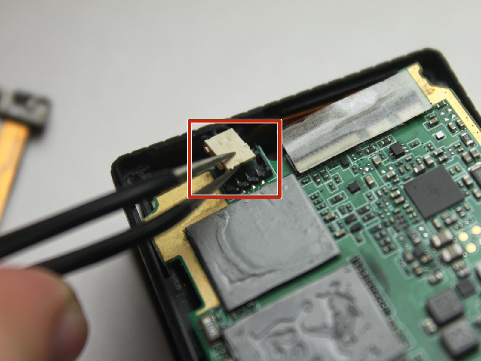 Olhar para o conector branco que tem dois fios que conduzem a partir da placa mãe para o compartimento de bateria na caixa da câmara.