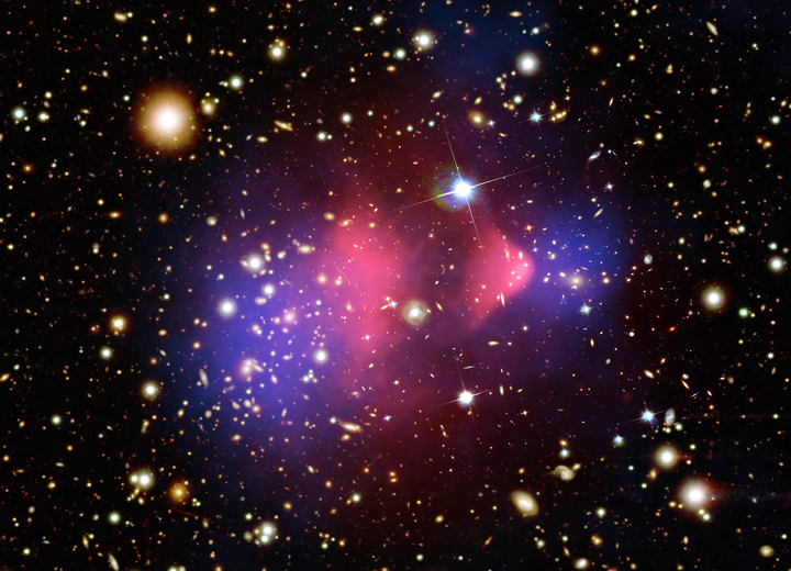 Figura 1.4: Imagem composta do Bullet Cluster 1E 0657-558. A região vermelha central corresponde a matéria bariônica na forma de plasma. As regiões azuis a os extremos representam a matéria escura.