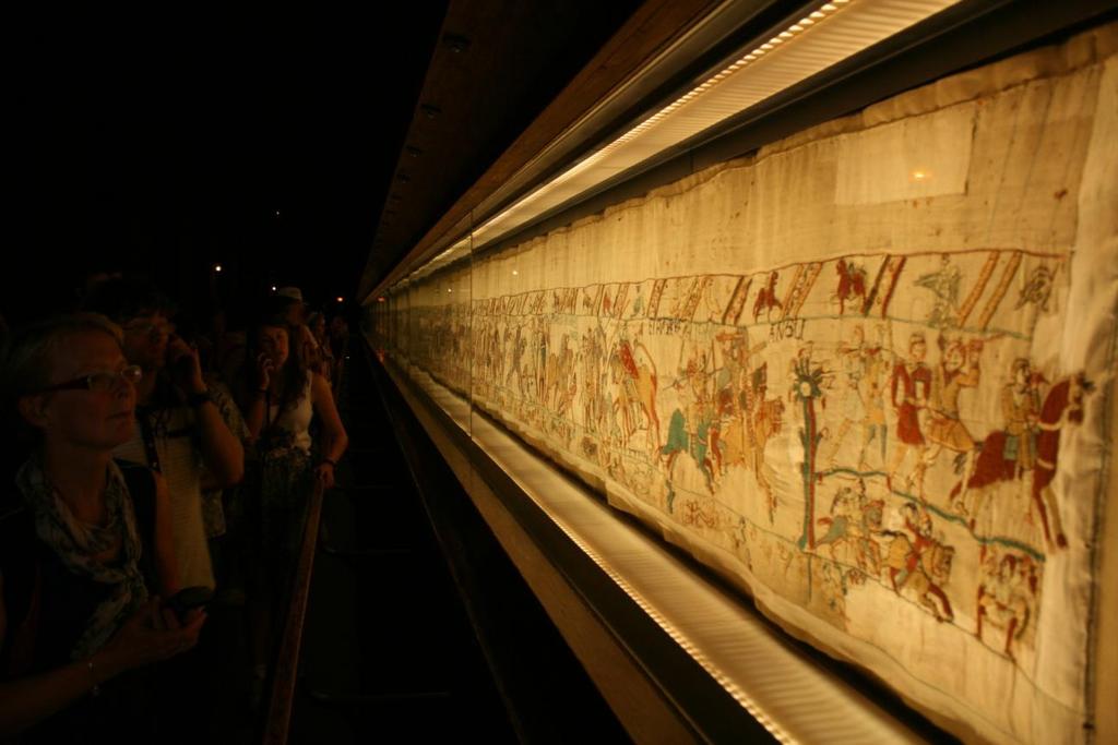 Imagem 18: Visitantes no Musée de la Tapisserie de Bayeux, onde a Tapeçaria de Bayeux se encontra na Normandia. Nota-se a disposição das imagens na tapeçaria como uma narrativa.