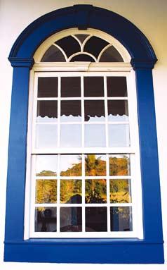 As janelas apresentam guilhotinas externas brancas em caixilhos de vidro com bandeira fixa com vidros coloridos e folhas internas enrelhadas, também brancas (f04