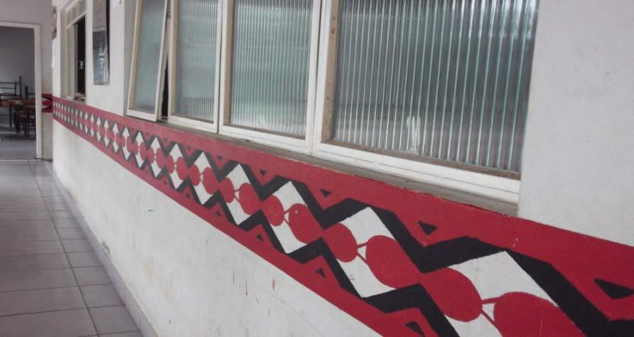 traço. Na foto a seguir, os alunos retratam os símbolos da etnia, sob um trabalho interdisciplinar registraram sua arte nas paredes da escola da aldeia.