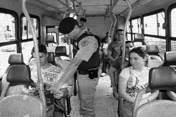 PRÁTICA POLICIAL BÁSICA Figura 25- PM Revistador no corredor do compartimento traseiro, vistoriando bagagem de passageiro. Ônibus com roleta.