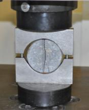 A resistência à tração determinada por compressão diametral foi realizada em corpos-de-prova cilíndricos de 100mm de diâmetro por 25mm de altura, montados em uma estrutura de aço (mordentes) com