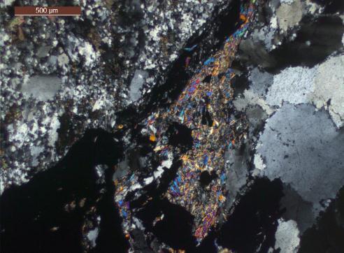 Descrição Veio de 30 cm de quartzo fumê. Quartzo (Qtz): é apresentado em dois tipos (I) cristais de granulação media a grossa (>600 µ) com extinção ondulante e bordas irregulares e lobadas.