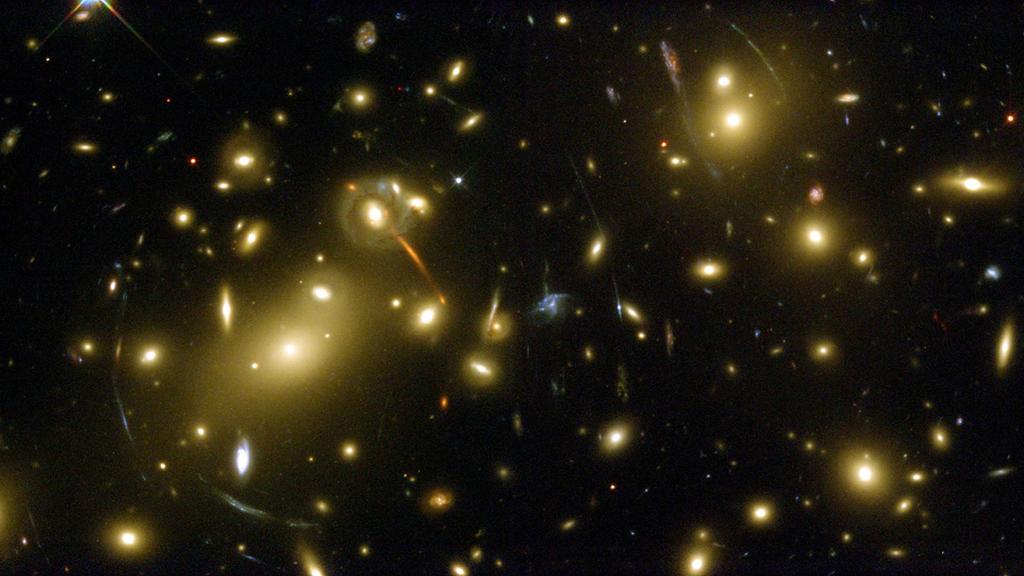 Estimativa de massa de aglomerados pelo lenteamento gravitacional O fenômeno de lenteamento gravitacional é utilizado para mapear a distribuição total de matéria em galáxias e aglomerados; Permitem