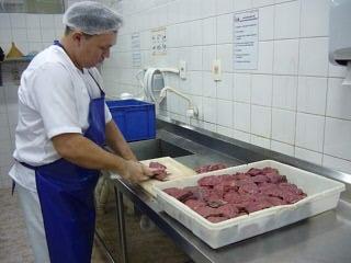 Colaborador em pé realizando o corte da carne sem riscos identificados.