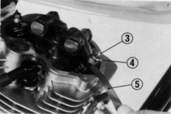 Verifique a folga das válvulas introduzindo um cálibre de lâminas (5) entre o parafuso de ajuste (3) e a haste das válvulas. Folga recomendada. Admissão: 0,08 mm Escape 0,08 mm.