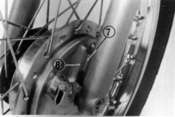 Posicione a roda dianteira entre os amortecedores alinhando a ranhura do flange do freio (8) com a guia do amortecedor esquerdo (7). 2.