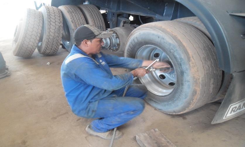 Colaborador realiza flexão de joelhos ficando de agachado ao fazer manutenção em pneu.