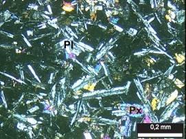 b) Descrição microscópica: a principal textura é a porfirítica, caracterizada pela presença de fenocristais de plagioclásio e clinopiroxênio, com dimensões variáveis entre 0,2 a 0,4 mm, imersos em
