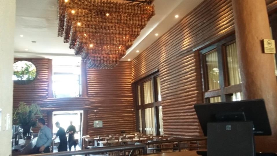 Figura 12: Imagem interna do restaurante mostrando a luminária e as paredes de adobe ensacado Fonte: Acervo próprio, 2017. O piso é feito em peças cerâmicas em tom bege com acabamento fosco.