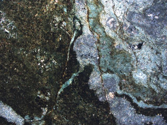 Apatite is abundant and closely associated to the amphiboles. B) Photomicrograph showing the detail of amphibole-biotite alteration zone crosscutting the biotite-chlorite alteration.
