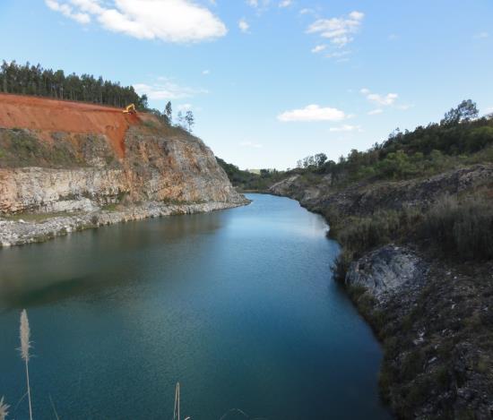 Neste ponto, a foto mostra o lago formado na cava de onde foi realizada a extração do minério e o trabalho de recuperação ambiental sendo