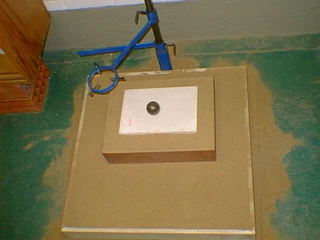 Para o ensaio, o corpo-de-prova é colocado sobre uma caixa de madeira preenchida com areia seca, que por sua vez também deverá estar sobre outra caixa de madeira preenchida com areia, de dimensões