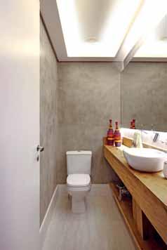 Moderno e despojado, o lavabo tem parede em cimento queimado, bancada de madeira de demolição e uma agradável iluminação indireta na sanca e espelho Na varanda, sutilmente mais rústica, o
