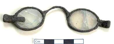 ÓCULOS 1361 JFM/00-3-26 O exemplar da Junta de Freguesia, em exposição no núcleo arqueológico local, exibe lentes ovais duplas fechadas na armação em ferro, com suportes laterais