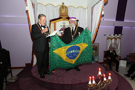 Grande Comendador Jorge Luiz de Andrade Lins, 33, ofertando-lhe uma linda toalha de mesa, no formato da Bandeira do Brasil, delicadamente confeccionada à mão, por meses, por bordadeiras paraguaias.