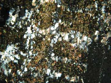 O quartzo apresenta contatos angulares e serrilhados, cristais subedrais a anedrais, e de dimensões aproximadas de 1,5 mm, quando formando bandas junto com a granada, e de 0,6 mm no restante.