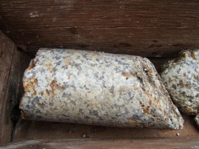 A rocha ácida, classificada como granito-gnaisse, tem composição essencialmente quartzo-feldspática, de granulação média a grossa.