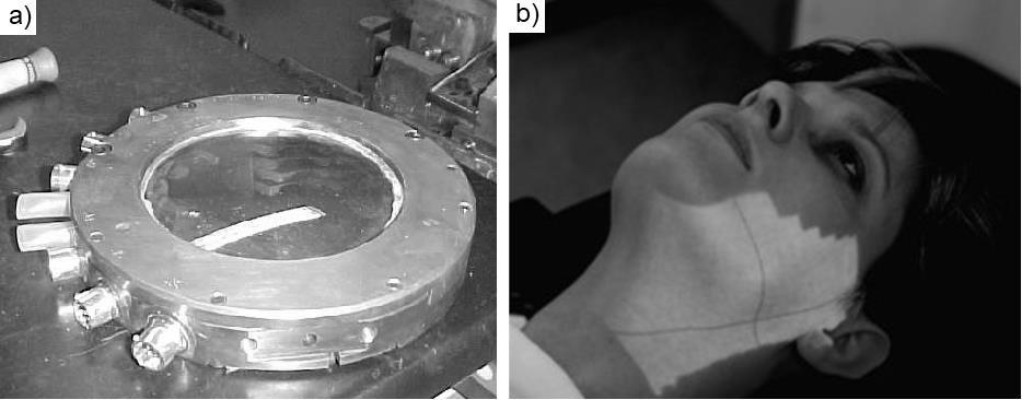 Figura 3.6 (a) Câmara de ionização de um linac sobre uma bancada de manutenção. (b) Projeção luminosa do campo de irradiação obtida com o uso do espelho de mylar.