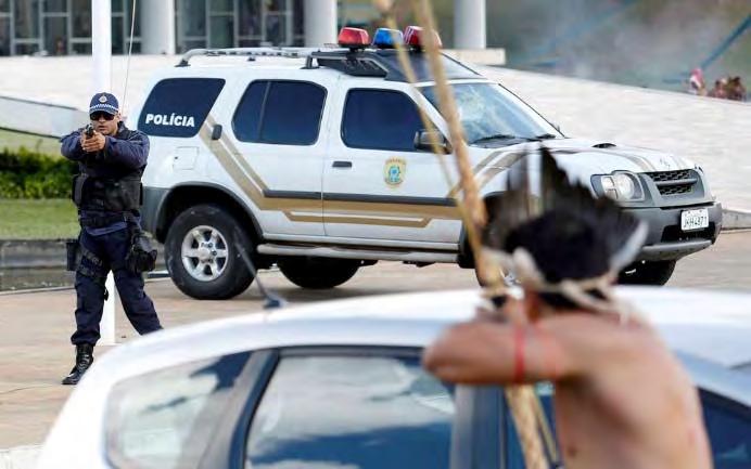 Um policial com uma arma em confronto com um indígena munido de arco e flecha durante os protestos ocorridos em Brasília/DF.