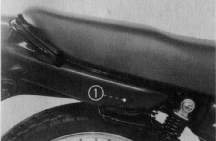 Trava do assento O assento de sua motocicleta está equipado com duas travas. Para remover o assento, introduza a chave de ignição no suporte do capacete e solte a presilha de segurança.