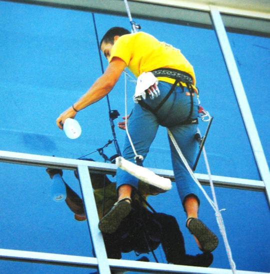 TÉCNICA DE ACESSO POR CORDA Operário, limpando vidraça, suportado apenas por uma corda, utilizando cinto de alpinismo, e equipamentos não adequados para o serviço.
