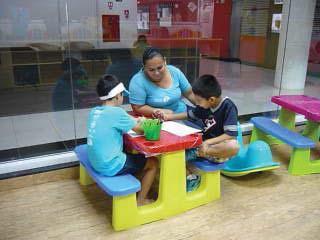 Colaboradora na posição sentada com as crianças, orientando as mesmas na execução das atividades lúdicas.
